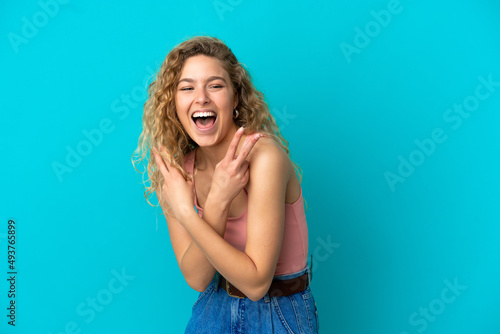Young blonde woman isolated on blue background smiling and showing victory sign © luismolinero