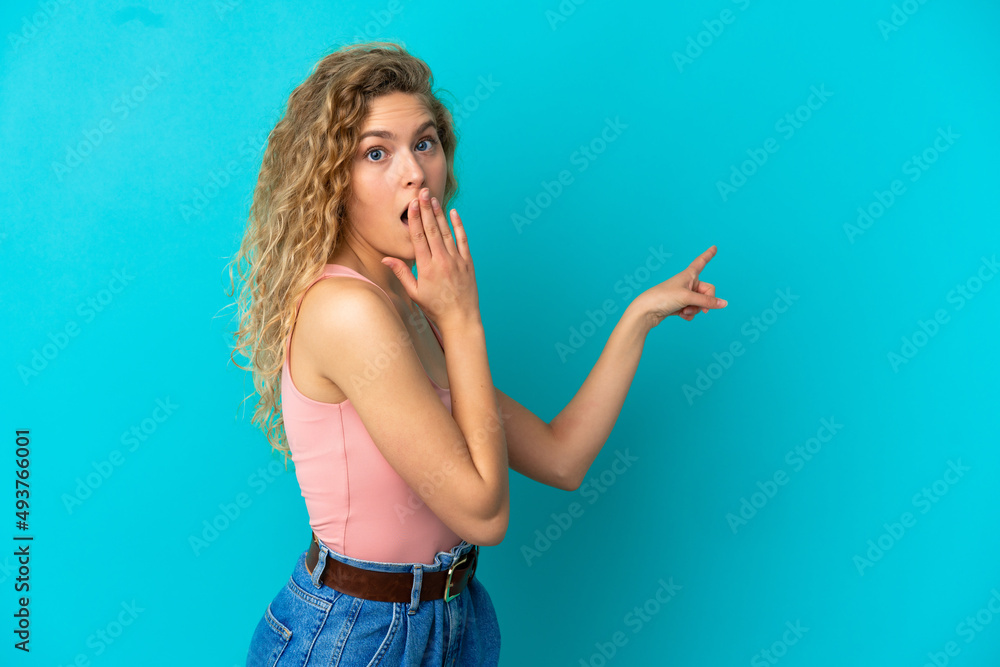 Fototapeta premium Young blonde woman isolated on blue background with surprise expression while pointing side