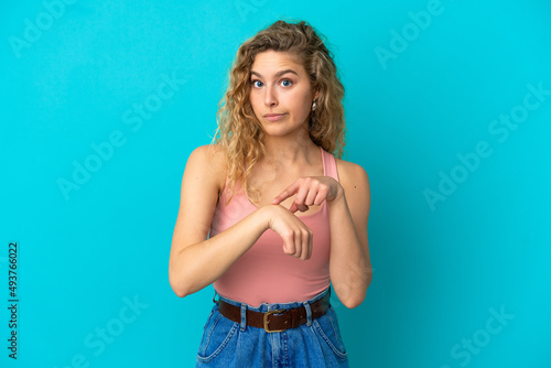 Young blonde woman isolated on blue background making the gesture of being late © luismolinero