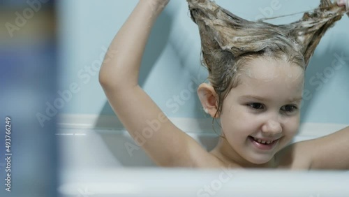 teenage girl caucasoid cute baby bathes in the bathtub and lathers the hair of the head, smiles beautifully. Slow motion, Portet. photo