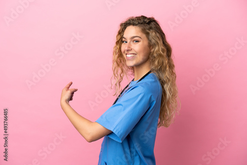 Young surgeon doctor woman isolated on pink background pointing back © luismolinero
