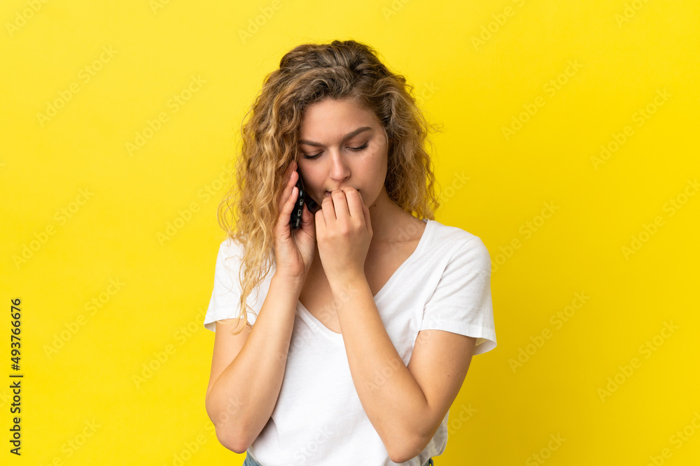 Young blonde woman using mobile phone isolated on yellow background having doubts Young blonde woman using mobile phone isolated on yellow background having doubts