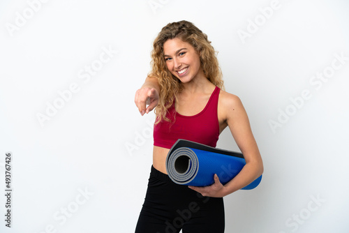 Young sport blonde woman going to yoga classes while holding a mat isolated on white background pointing front with happy expression