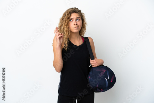 Young sport woman with sport bag isolated on white background with fingers crossing and wishing the best