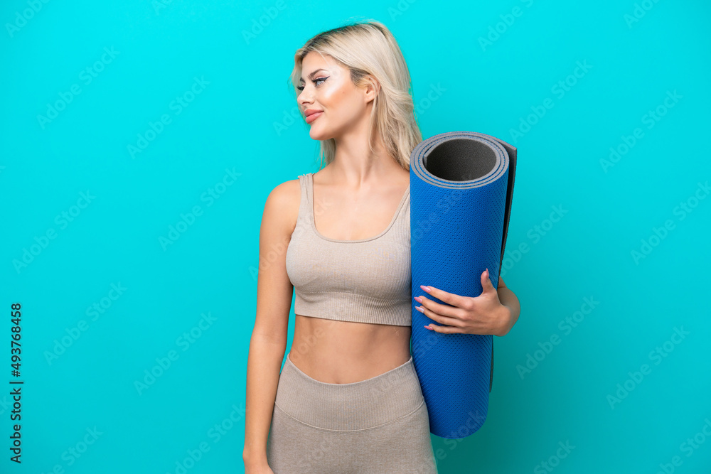 Sport woman going to yoga classes while holding a mat isolated on blue background looking side Sport woman going to yoga classes while holding a mat isolated on blue background looking side