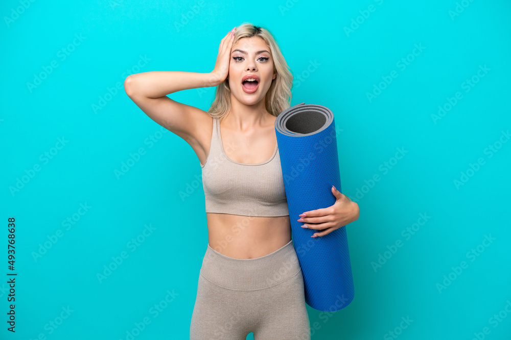 Sport woman going to yoga classes while holding a mat isolated on blue background with surprise expression Sport woman going to yoga classes while holding a mat isolated on blue background with surprise expression
