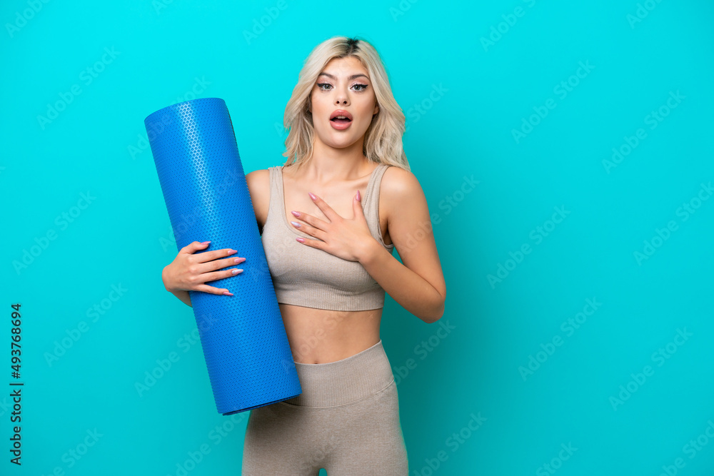 Sport woman going to yoga classes while holding a mat isolated on blue background surprised and shocked while looking right Sport woman going to yoga classes while holding a mat isolated on blue background surprised and shocked while looking right