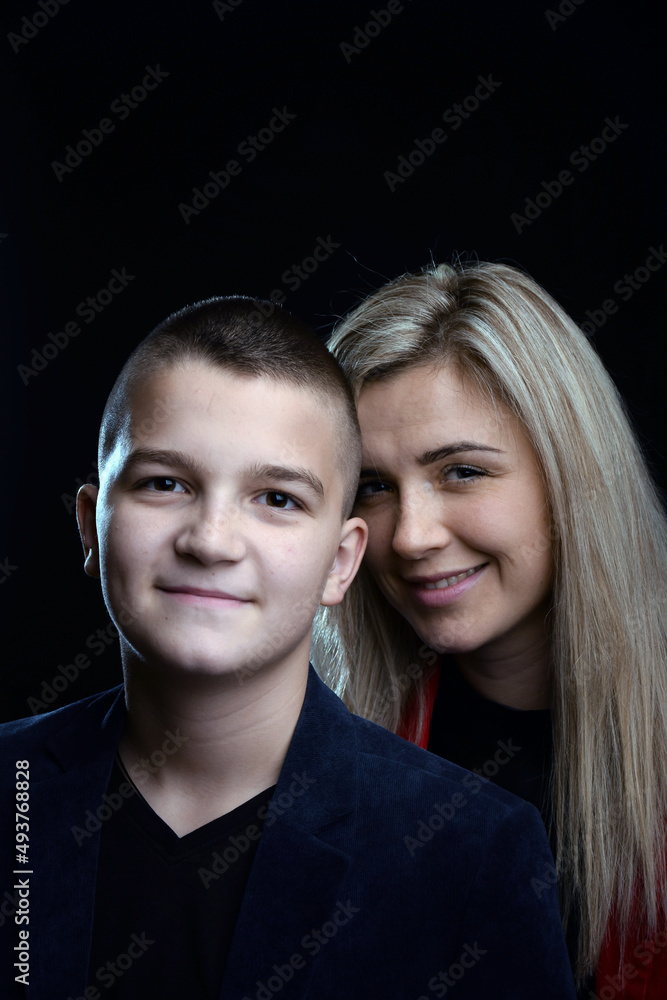 A young attractive mother is standing behind her white teenage son and both are smiling. Studio photo on a dark background A young attractive mother is standing behind her white teenage son and both are smiling. Studio photo on a dark background
