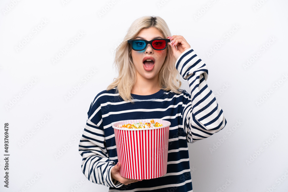 Obraz premium Young Russian woman isolated on white background surprised with 3d glasses and holding a big bucket of popcorns