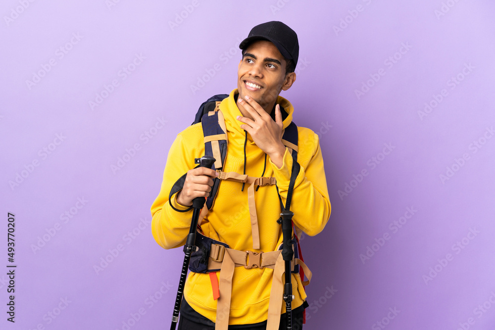 African American man with backpack and trekking poles over isolated background looking up while smiling African American man with backpack and trekking poles over isolated background looking up while smiling