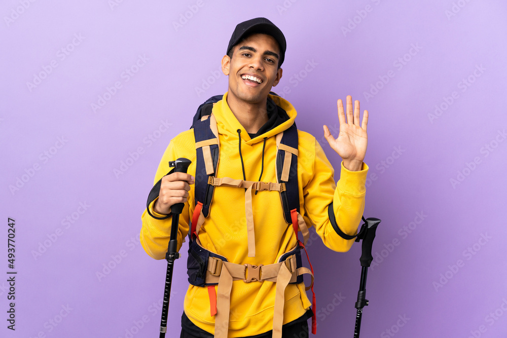 African American man with backpack and trekking poles over isolated background saluting with hand with happy expression African American man with backpack and trekking poles over isolated background saluting with hand with happy expression