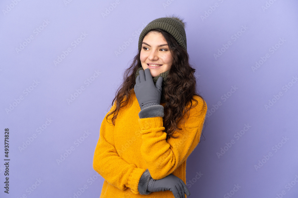 Teenager Russian girl with winter hat isolated on purple background looking up while smiling Teenager Russian girl with winter hat isolated on purple background looking up while smiling