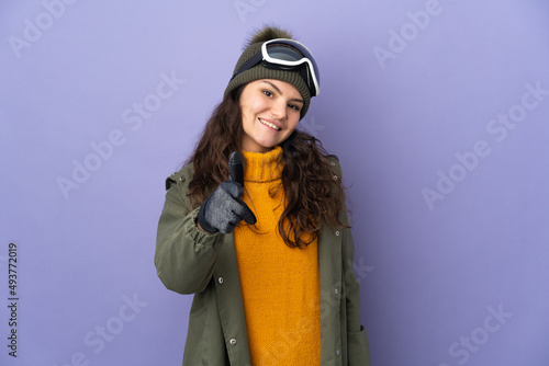 Teenager Russian girl with snowboarding glasses isolated on purple background pointing front with happy expression © luismolinero