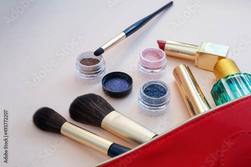 Top view of cosmetics standing out from red cosmetic bag on pink background