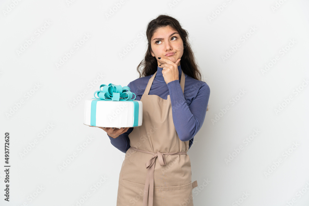 Pastry Russian chef holding a big cake isolated on white background having doubts Pastry Russian chef holding a big cake isolated on white background having doubts