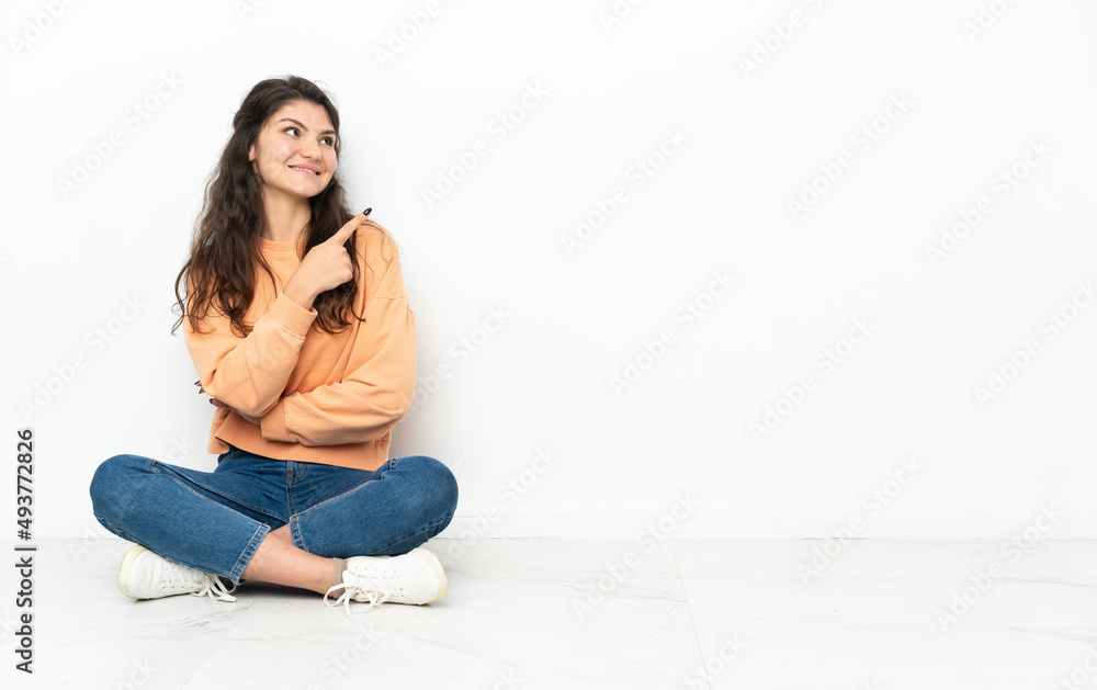Teenager Russian girl sitting on the floor pointing up a great idea