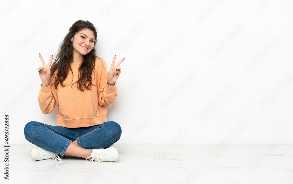 Teenager Russian girl sitting on the floor showing victory sign with both hands Teenager Russian girl sitting on the floor showing victory sign with both hands