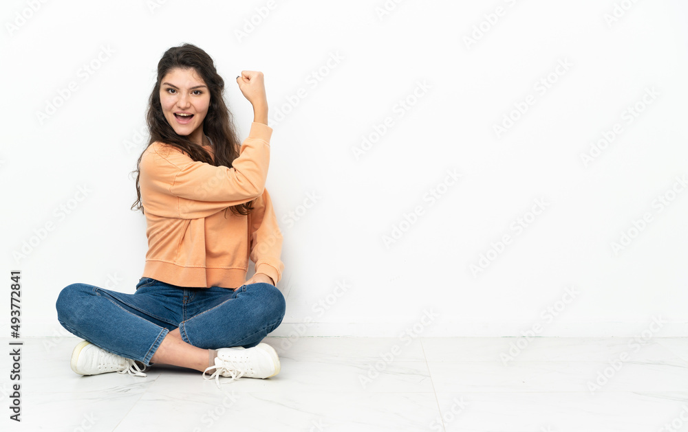 Teenager Russian girl sitting on the floor doing strong gesture