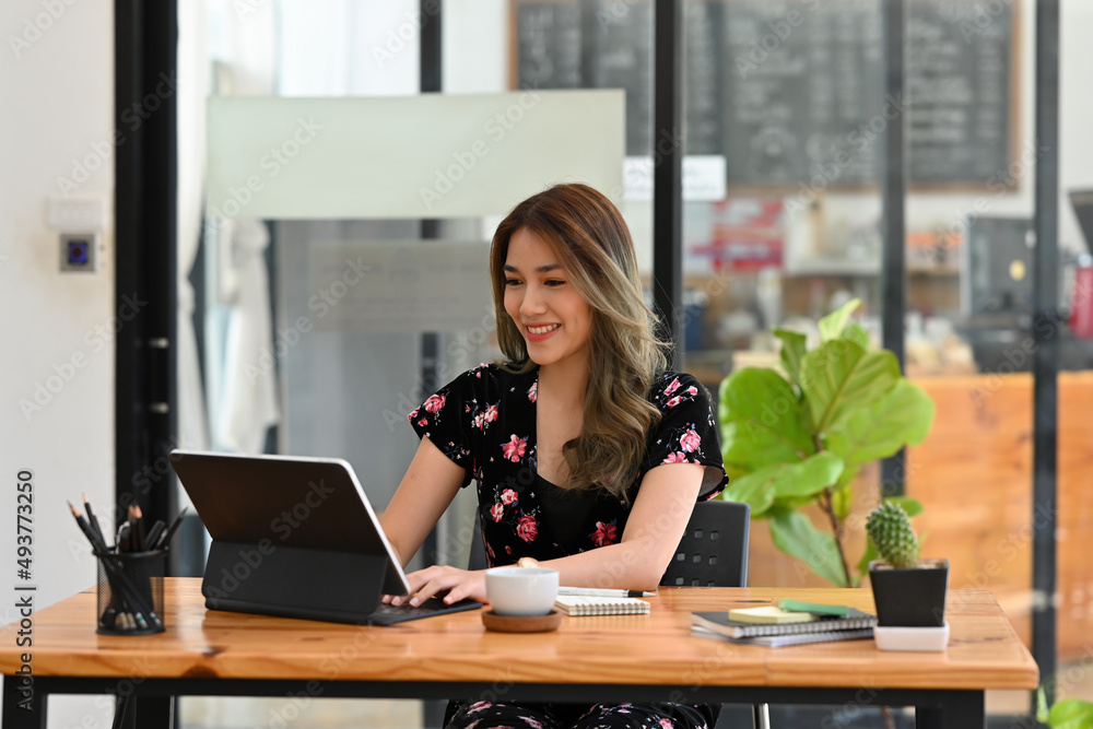 A portrait of a pretty smiley Asian woman sitting in the office looking at a tablet and working on a document, for business and technology concept. A portrait of a pretty smiley Asian woman sitting in the office looking at a tablet and working on a document, for business and technology concept.