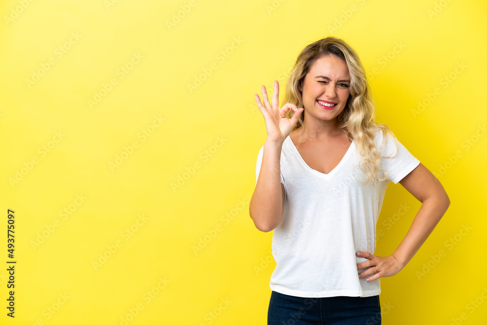 Young Brazilian woman isolated on yellow background showing ok sign with fingers Young Brazilian woman isolated on yellow background showing ok sign with fingers
