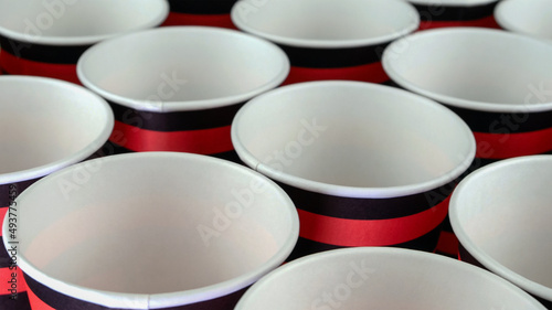 Row of red and black disposable eco friendly paper cup for coffee or hot beverage on dark backdrop. Selective focus.
