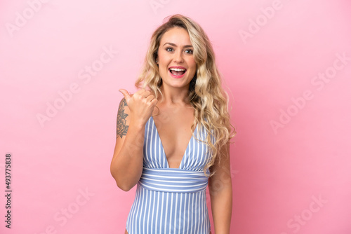 Young Brazilian woman in swimsuit in summer holidays isolated on pink background pointing to the side to present a product