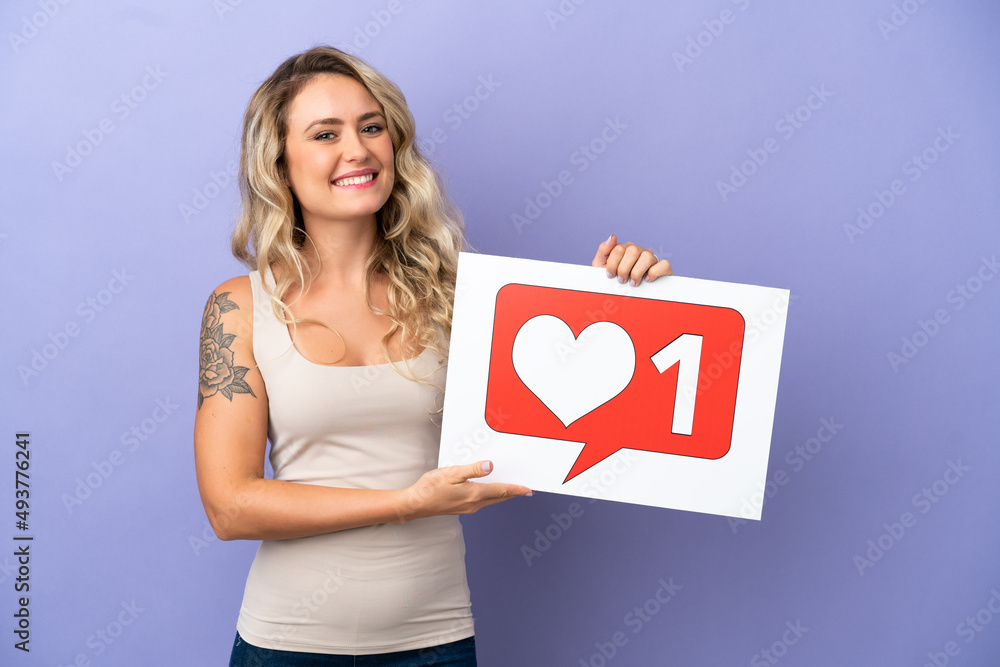 Young Brazilian woman isolated on purple background holding a placard with Like icon with happy expression Young Brazilian woman isolated on purple background holding a placard with Like icon with happy expression