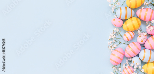 Easter holiday background with colorful easter eggs and white flowers on blue background.