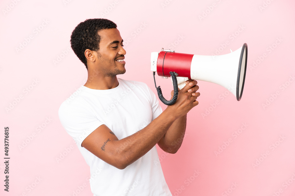 African American handsome man on isolated pink background shouting through a megaphone to announce something African American handsome man on isolated pink background shouting through a megaphone to announce something