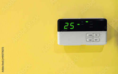 25 celsius of room is comfort temperature and energy saving. Digital remote controller of the air conditioning on yellow wall. Electric consumption.