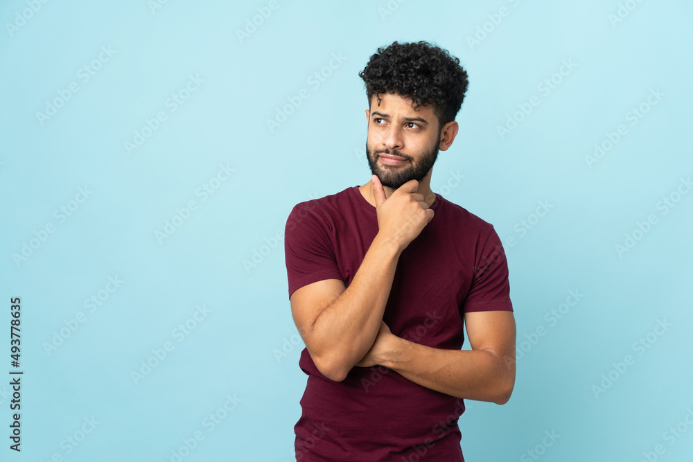 Young Moroccan man isolated on blue background and looking up Young Moroccan man isolated on blue background and looking up