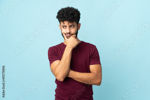Young Moroccan man isolated on blue background having doubts