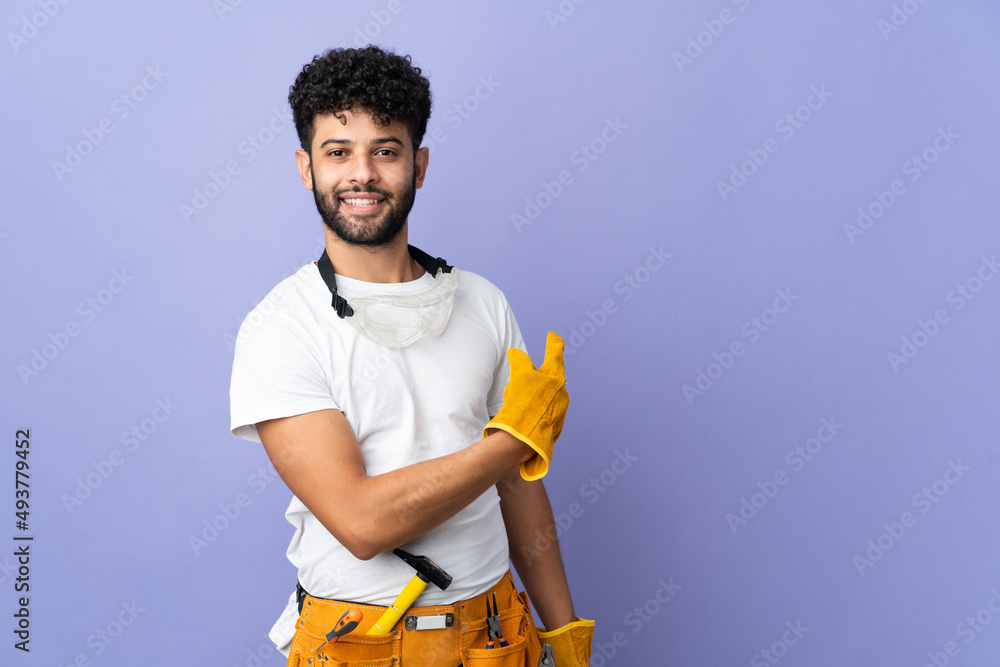 Young electrician Moroccan man isolated on purple background pointing back Young electrician Moroccan man isolated on purple background pointing back