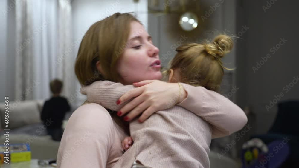 Young mother calms, hugs and kisses an irritated daughter in her arms in a large living room Young mother calms, hugs and kisses an irritated daughter in her arms in a large living room