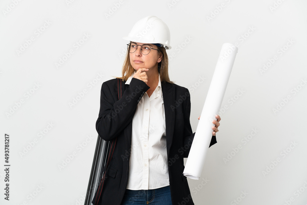 Middle age architect woman with helmet and holding blueprints over isolated background and looking up Middle age architect woman with helmet and holding blueprints over isolated background and looking up