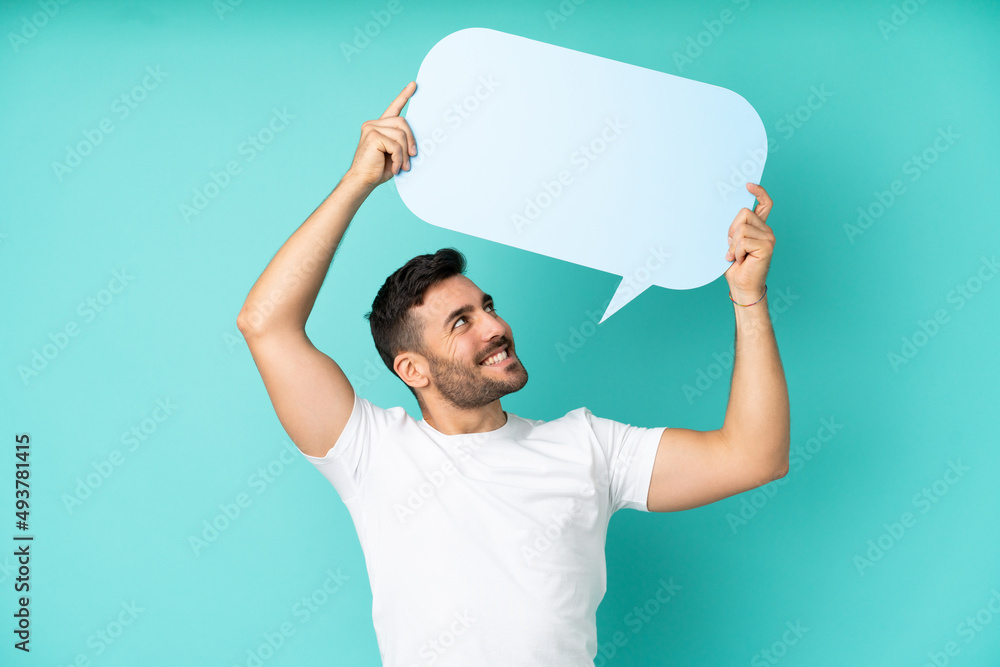 Young handsome caucasian man isolated on blue background holding an empty speech bubble Young handsome caucasian man isolated on blue background holding an empty speech bubble
