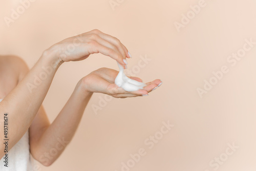 Lush foam for washing the face in the hands of a woman. Close up on a beige background.