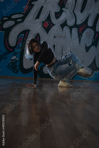 Female dancer in activewear squatting on the floor of modern dance studio and looking at you