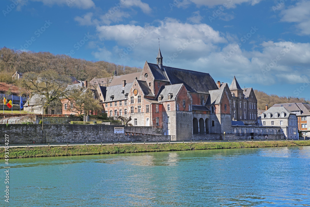 Fototapeta premium Dinant, Belgium - March 9. 2022: View over river meuse on medieval government building cpas aiginst blue sky, fluffy clouds