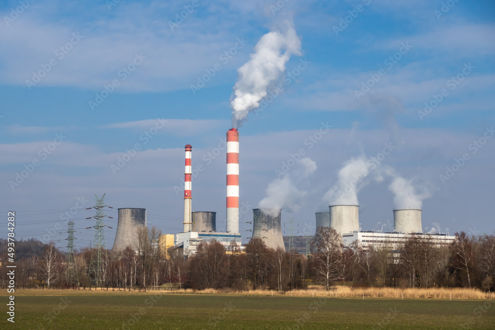 Distant view of a coal-fired power plant. Smoking chimneys and steam from cooling towers. Photo taken on a sunny day, Contrast lighting.