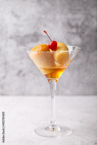 Neapolitan Rum baba (or baba au rum) in a martini glass with a cocktail cherry on a gray background. Small yeast cakes soaked in rum syrup. Traditional Italian pastry. Close-up, selective focus.