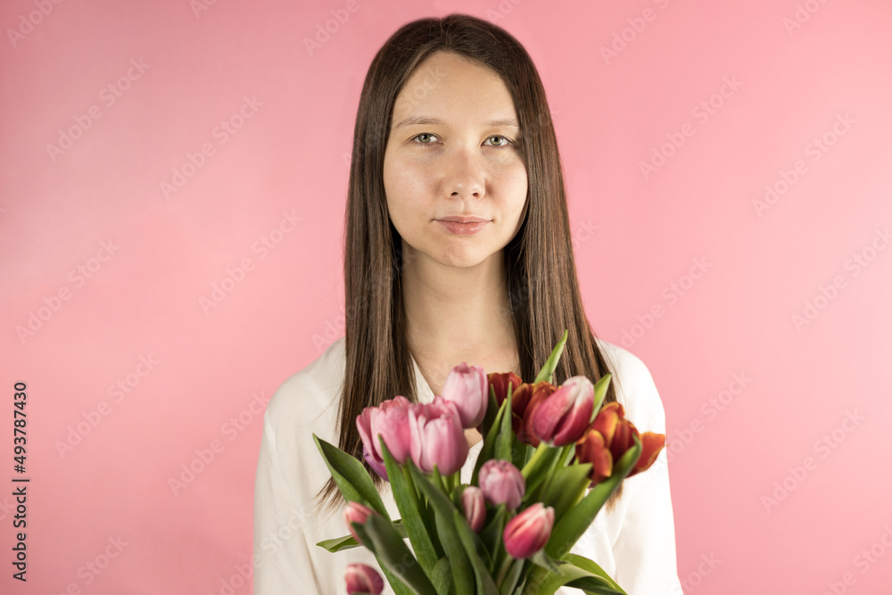 Close-up portrait of a beautiful brunette girl holding a bouquet of tulips isolated on a pastel pink background. Concept: mother's Day, Women's Day. Give the girls flowers