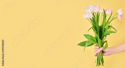 Woman hand holds tulip flowers bouquet on yellow background with copy space