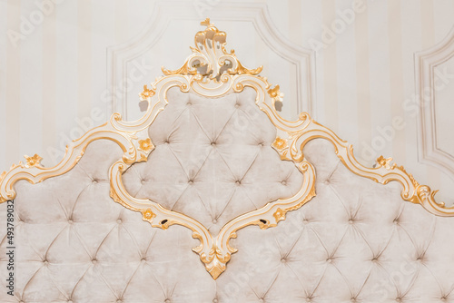 Luxury royal headboard of expensive bed with golden elements and light beige textile - elegant part of bedroom interior