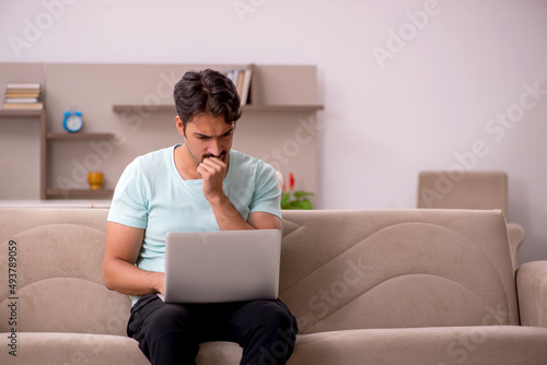 Young man sitting on the sofa with computer at home © Elnur