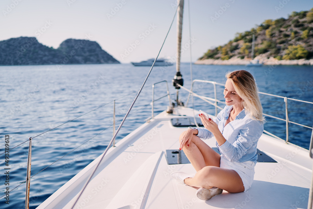Luxury travel on the yacht. Young happy woman using smartphone on boat deck sailing the sea. Yachting and technology.