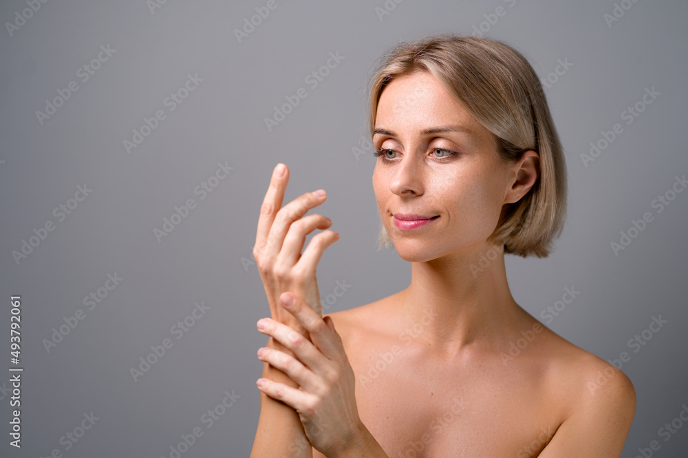 Skin care. Blonde woman with beauty face touching hands. No makeup. Grey background. Skin care. Blonde woman with beauty face touching hands. No makeup. Grey background.