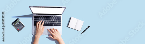 Person using a laptop computer with a notebook and a calculator