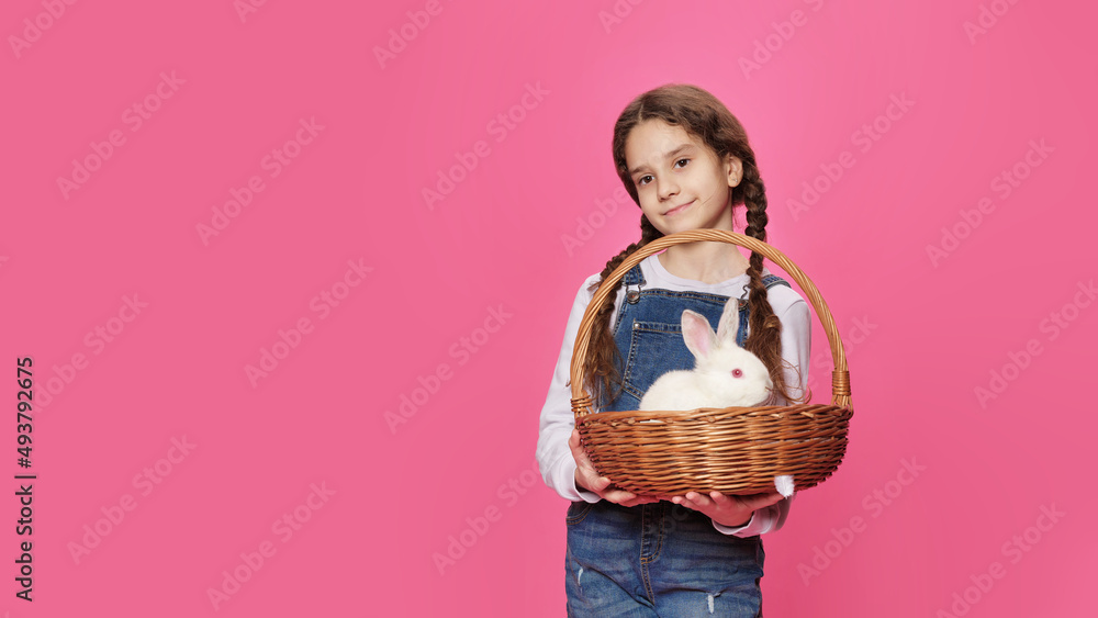 Cute schoolgirl holds a basket with a real rabbit, poses in the studio, on a pink background. Cute schoolgirl holds a basket with a real rabbit, poses in the studio, on a pink background.
