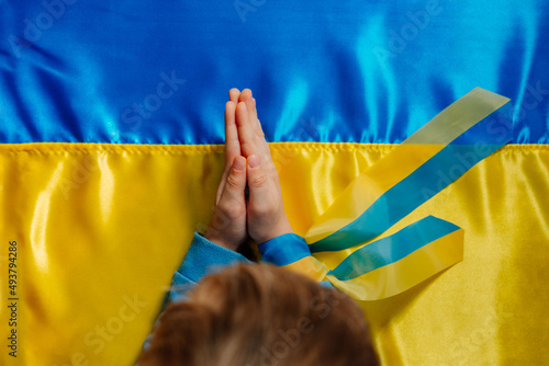 Kids handswith ribbon praying on the Ukrainian flag photo